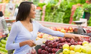 Woman shopping for fresh produce in a grocery store, selecting apples for a healthy IBD-friendly diet