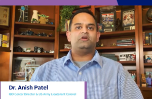 Man with a serious expression in a blue checkered shirt stands in front of a bookshelf filled with books and memorabilia. Text: "Dr. Anish Patel, IBD Center Director & US Army Lieutenant Colonel."