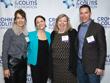 Four smiling staff members pose together at a Crohn’s & Colitis Foundation event, standing before a branded backdrop in a friendly, celebratory mood.