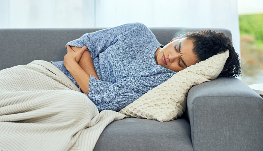 a woman curled up on er couch ion pain grasping her stomach